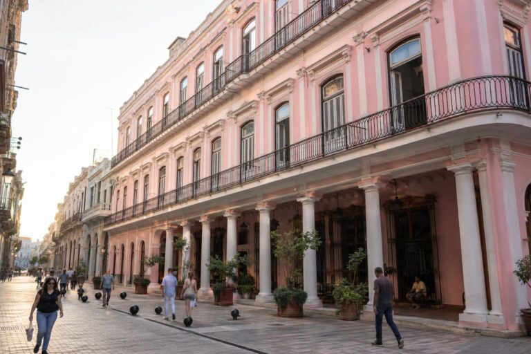 Pink Hotel Ambos Mundos façade with rows of windows above pedestrians on a narrow Old Havana street.