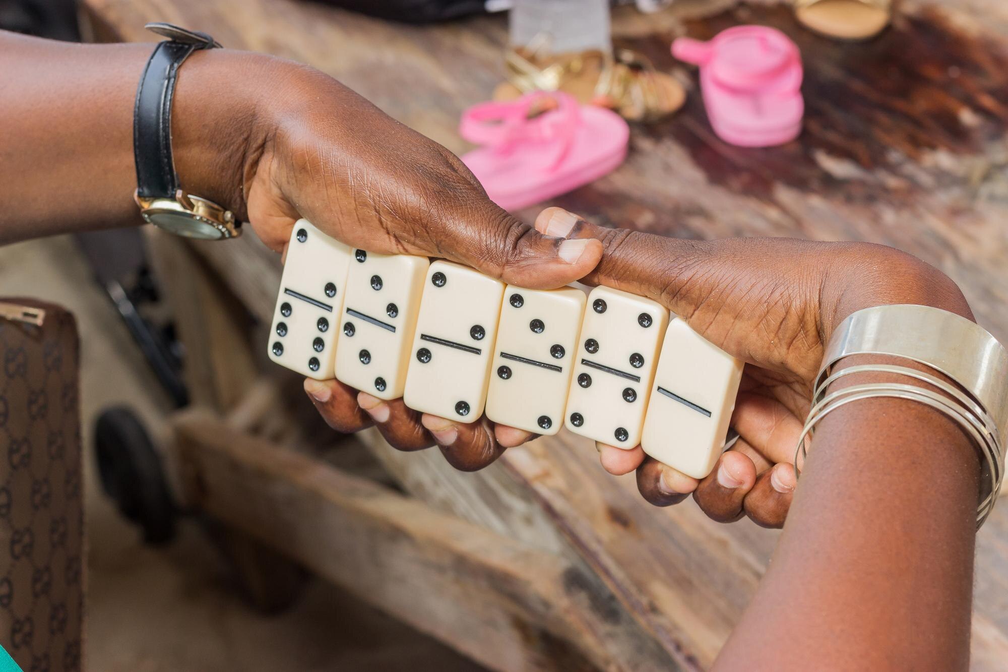 Hands holding domino tiles above a worn wooden table.