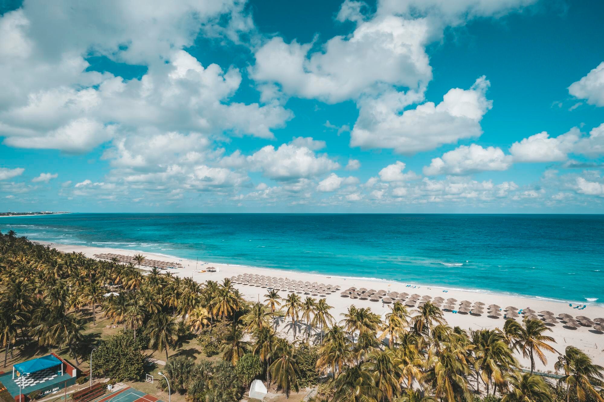 White-sand beach lined with palms and straw umbrellas beside turquoise water in Varadero, Cuba.